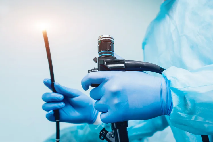 A specialist in blue surgical gloves holding an endoscope, a flexible tube with a light and camera used for colonoscopy and endoscopy.
