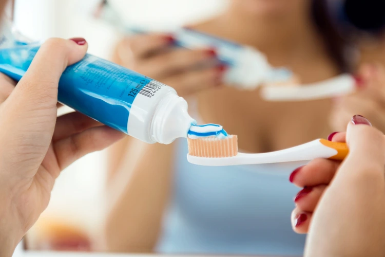 Lady squeezing out toothpaste onto her toothbrush to brush her teeth.