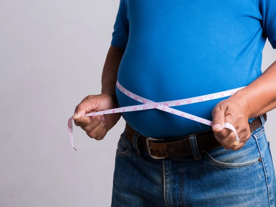 Man suffering from obesity with a large tummy measuring his waist size.