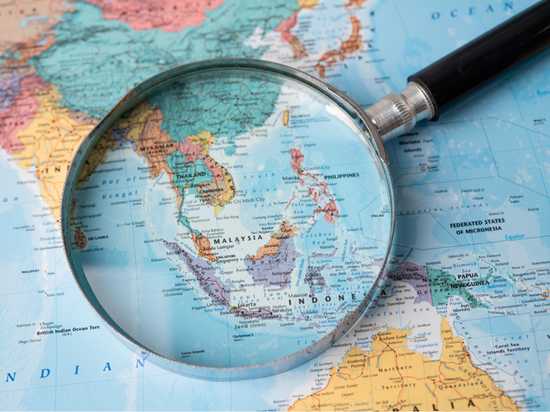 Magnifying glass highlighting South East Asia on world map for travel planning.