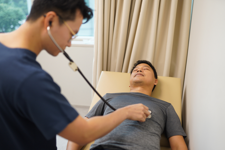 Doctor using stethoscope to check patient during pre-employment medical examination at clinic.
