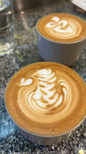 Latte art in modern cups at Equate Coffee Singapore with intricate foam designs.