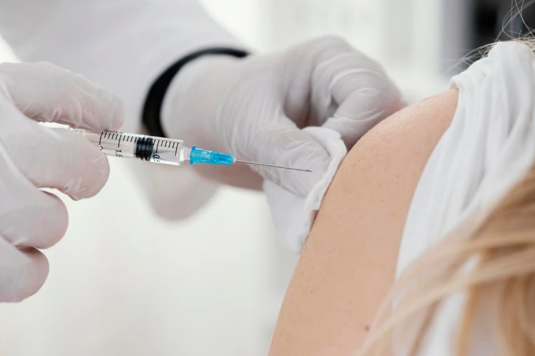 Nurse administering meningococcal vaccine jab to female patient.