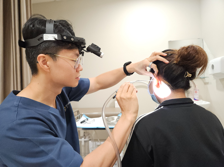 Doctor at ATA Medical performing microsuction ear wax removal under direct visualisation with a headlamp and magnifying loupe.